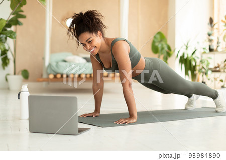 Excited athletic african american lady exercising at home, sporty black woman enjoying online yoga class, using laptop 93984890