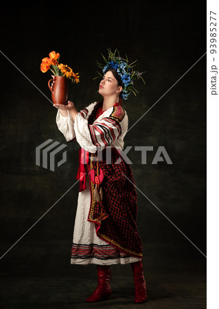 Art portrait of beautiful woman wearing traditional folk Ukrainian costume posing isolated over dark vintage background. Fashion, beauty, cultural heritage Art portrait of beautiful woman wearing traditional folk Ukrainian costume posing isolated over dark vintage background. Fashion, beauty, cultural heritage 93985277