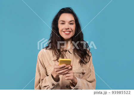 Portrait of happy millennial caucasian brunette woman in casual typing on smartphone Portrait of happy millennial caucasian brunette woman in casual typing on smartphone 93985522