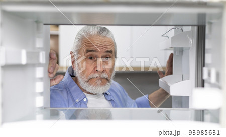 Hungry Senior Man Looking At Empty Shelves In Fridge At Home Hungry Senior Man Looking At Empty Shelves In Fridge At Home 93985631