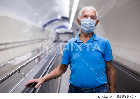 Retired man in protective mask walking down the escalator to metro station 93989757