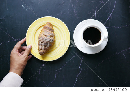 fresh baked croissant on plate and cup of tea on black background  93992100
