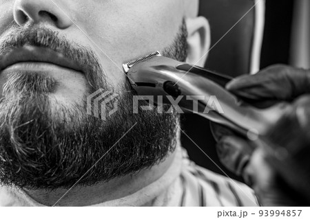 Man getting his beard trimmed with electric razor in barbershop. Black and white image. 93994857