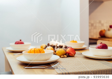 Fall table setting for celebration Thanksgiving day family party. Autumn composition with candles, fruits, nuts and cones. Plates with pumpkins and pomegranate. Natural autumn decor. Selective focus Fall table setting for celebration Thanksgiving day family party. Autumn composition with candles, fruits, nuts and cones. Plates with pumpkins and pomegranate. Natural autumn decor. Selective focus 93995630