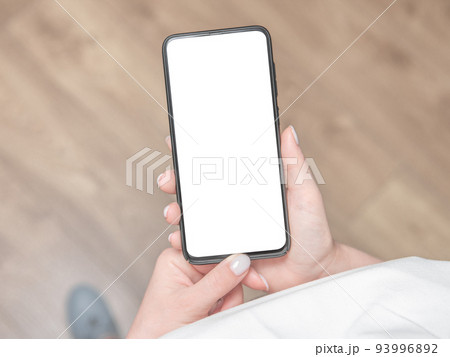 Woman stands and holds a mobile phone with a blank screen in her hands. 93996892