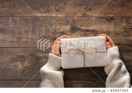 woman holding christmas gift box. Wooden rustic table. Top view woman hands holding present box 93997305