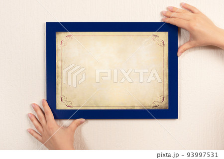 mockup diploma. woman hanging old certificate mockup on wall. White frame mockup 93997531