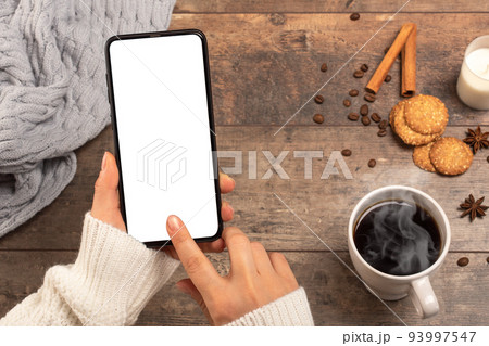 Mockup image of woman's hands holding mobile phone with blank white desktop screen while drinking coffee in cafe. cold weather, winter season 93997547