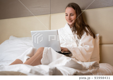 Brown-haired woman types messages to friend on laptop Brown-haired woman types messages to friend on laptop 93998431