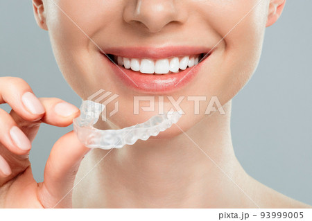 The woman holds in her hand removable invisible transparent aligners, and smiles. 93999005