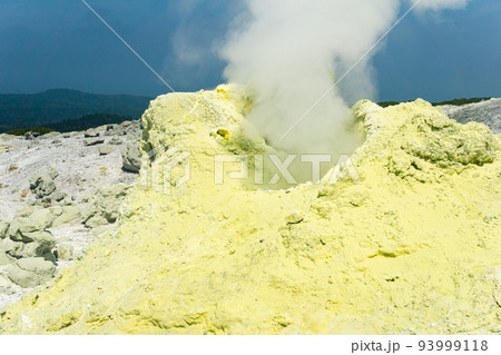 cone of sulfur deposits around a fumarole in a solfataric field illuminated by the sun against a stormy landscape in the distance cone of sulfur deposits around a fumarole in a solfataric field illuminated by the sun against a stormy landscape in the distance 93999118