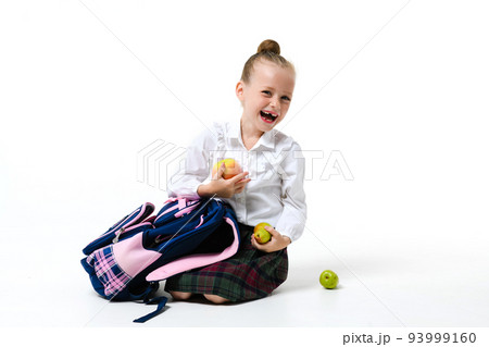 Cute girl in school uniform with a backpack and apples on a white background. 93999160