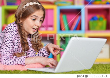 Teenage girl with laptop lying on carpet at home 93999491