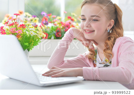 Teenage girl sitting at a table with a laptop 93999522