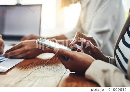 Closeup of a businesswoman hands on the phone texting colleagues, replying to messages or social media. Marketing professional female taking a break from working together with her team on a project 94000852
