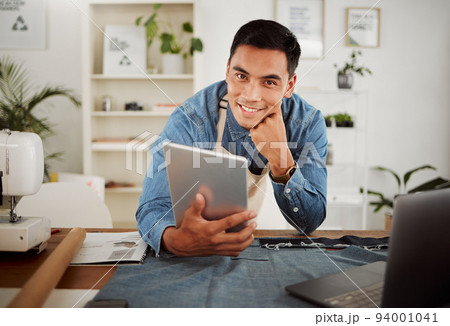 Looking for fashion design ideas on tablet, planning creative clothing and working on website online while in a factory at work. Portrait of smiling designer, stylist or tailor at a shop for clothes 94001041