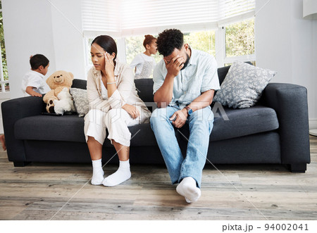 Sad, unhappy and stressed parents sitting on a couch near their children at home after an argument. Frustrated, tired and annoyed mom and dad are angry at hyperactive, noisy and naughty kids 94002041