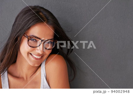 Cool, confident and beautiful woman wearing glasses and smiling with a grey wall and copy space. Face of a cheerful, stunning, attractive and happy female feeling good and showing a positive attitude 94002948