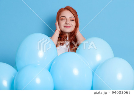 Pleased young redhead woman in white casual clothing covering ears with fingers isolated on color background, posing among air balloons, celebration, surprise on party, girl with smile and closed eyes Pleased young redhead woman in white casual clothing covering ears with fingers isolated on color background, posing among air balloons, celebration, surprise on party, girl with smile and closed eyes 94003065