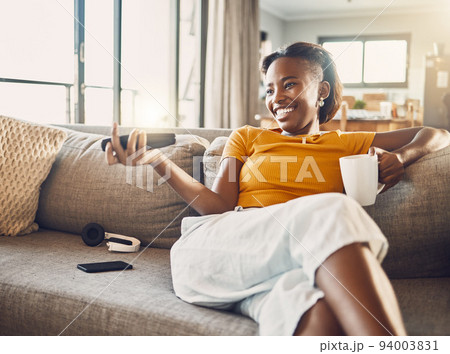 Relaxed, carefree and smiling young female watching tv and streaming movie at home on her living room sofa. Happy, casual and comfortable woman sitting on her couch and enjoying her leisure free time 94003831