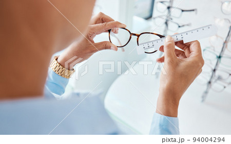 Optician or optometrist hands measuring and preparing pair of glasses and frame with optic ruler tool. Eye doctor or ophthalmologist determines visual or vision lens size using special eyewear scale. Optician or optometrist hands measuring and preparing pair of glasses and frame with optic ruler tool. Eye doctor or ophthalmologist determines visual or vision lens size using special eyewear scale. 94004294