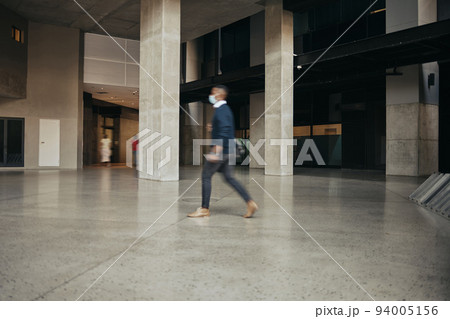 Covid travel regulations for a business man traveling and walking in an airport or hotel. Leaving the office building in hurry, being late or rushing after working overtime in a city or urban town Covid travel regulations for a business man traveling and walking in an airport or hotel. Leaving the office building in hurry, being late or rushing after working overtime in a city or urban town 94005156