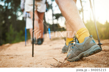 . Feet or shoes walking, trekking and hiking on a trail up a mountain with sticks and poles. Closeup of group of adventurous hikers or friends exploring rugged path on a mountain in nature. . Feet or shoes walking, trekking and hiking on a trail up a mountain with sticks and poles. Closeup of group of adventurous hikers or friends exploring rugged path on a mountain in nature. 94005215