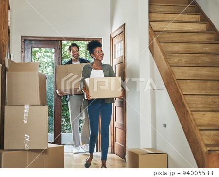 Interracial couple moving into a new modern house, carrying boxes and arriving home together. Happy, excited and smiling husband and wife walking, entering and relocating after buying an apartment 94005533