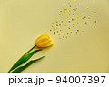 Spring tulip with fresh green leaves on a yellow background. Splashes of golden glitter. 94007397