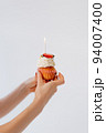 Delicious cake with cream and strawberries in elegant female hands. A sweet birthday present. A burning candle creates a holiday mood. 94007400
