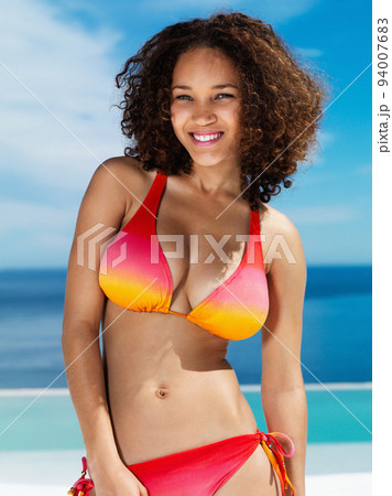 Portrait of happy and sexy woman in a bikini with curly hair at the beach in summer. Beauty model with a smile and ocean, water and blue sky in the background while on holiday, vacation or travel 94007683