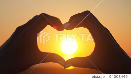 Woman makes big heart with hands at back sunset closeup Woman makes big heart with hands at back sunset closeup 94008446