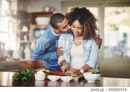 Romantic, loving and caring boyfriend embraces his girlfriend and shows affection while they make food in the kitchen. A couple sharing a kiss and hug while cooking a meal or salad at home. Romantic, loving and caring boyfriend embraces his girlfriend and shows affection while they make food in the kitchen. A couple sharing a kiss and hug while cooking a meal or salad at home. 94008458