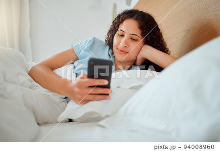 Woman texting, checking messages and holding phone while reading sms and lying awake in her bed in the morning. Happy, content and smiling female playing a game, browsing the internet or social media Woman texting, checking messages and holding phone while reading sms and lying awake in her bed in the morning. Happy, content and smiling female playing a game, browsing the internet or social media 94008960