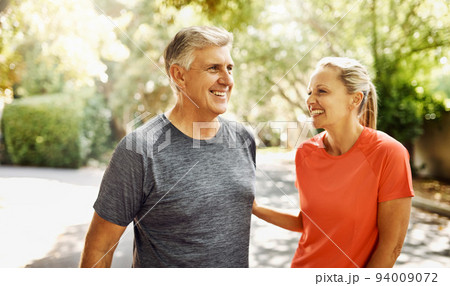 Happy mature couple keeping active, fit and healthy while jogging, running or going for walk outdoors in nature environment. Laughing senior man and woman enjoying a break from workout or exercising 94009072