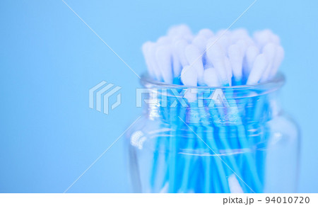 Glass container with cotton makeup cosmetic swab buds, self cleaning ear canal and environment recycle. Covid nasal test, skincare health safety and climate change on blue background closeup Glass container with cotton makeup cosmetic swab buds, self cleaning ear canal and environment recycle. Covid nasal test, skincare health safety and climate change on blue background closeup 94010720