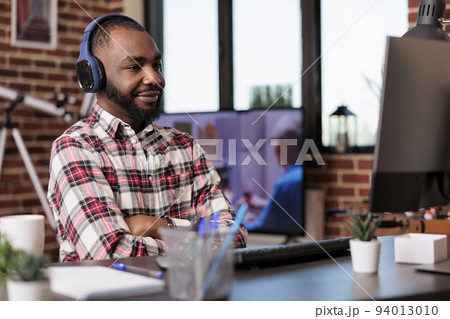 Male freelancer using headphones and working remotely on computer at home desk. Listening to music or podcast show online on social media internet, attending class lesson webinar. Male freelancer using headphones and working remotely on computer at home desk. Listening to music or podcast show online on social media internet, attending class lesson webinar. 94013010