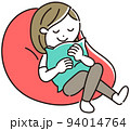 ビーズクッションに座り、クッションを抱いてリラックスする若い女性 94014764