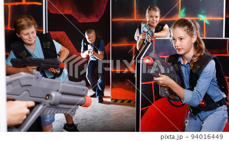 Happy teen brother and sister standing with laser pistols during laser tag game with parents in labyrinth Happy teen brother and sister standing with laser pistols during laser tag game with parents in labyrinth 94016449
