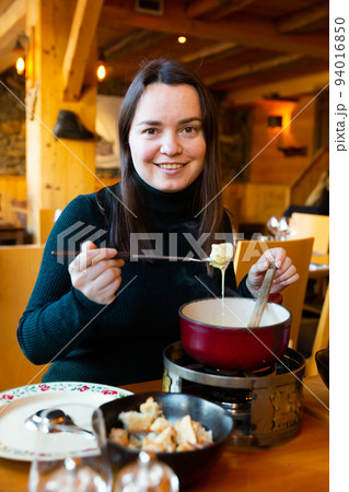 Young adult woman eating fondue at restaurant 94016850