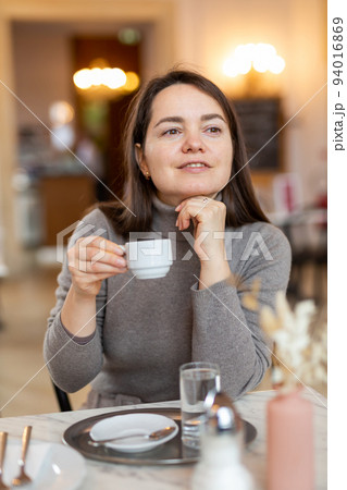 Brunette sitting in cozy cafe with cup of coffee Brunette sitting in cozy cafe with cup of coffee 94016869