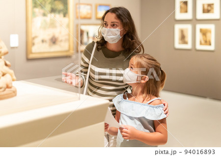 Mother and daughter in masks with guide enjoying expositions in museum 94016893