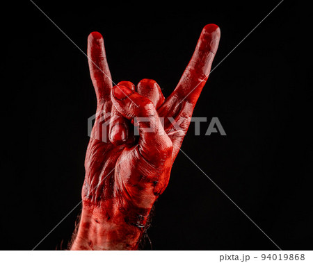 A man's hand covered in blood shows a goat sign on a black background. A man's hand covered in blood shows a goat sign on a black background. 94019868