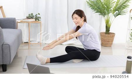 Beautiful Asian woman in sportswear is warming up or doing light exercises in the house with dumbbells and a protein shake or bottle of water and using a laptop at home, Healthy exercise. 94020554