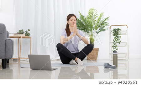 Beautiful Asian woman in sportswear is warming up or doing light exercises in the house with dumbbells and a protein shake or bottle of water and using a laptop at home, Healthy exercise. 94020561