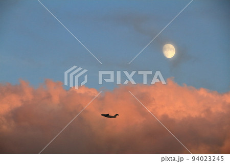 秋の夕暮れ　夕日に染まる雲と月と訓練飛行中のC-2輸送機 94023245