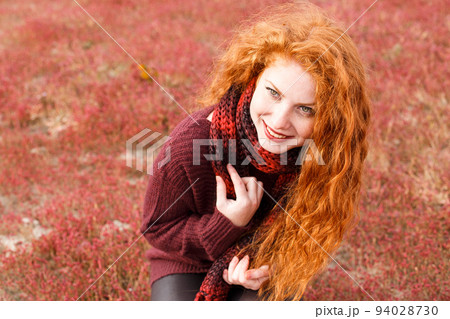 Red girl in burgundy sweater, scarf sits in field in wind smiling on frame 94028730