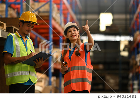 Warehouse workers in hardhats and and vests inspecting stock tick on digital tablet in a large warehouse Warehouse workers in hardhats and and vests inspecting stock tick on digital tablet in a large warehouse 94031481
