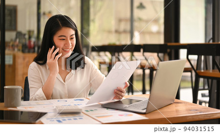 Professional female advisor reading document and consulting client on cellphone at her office desk 94031515