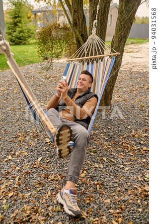 Joyful dark-haired male using his cellphone outdoors 94031568